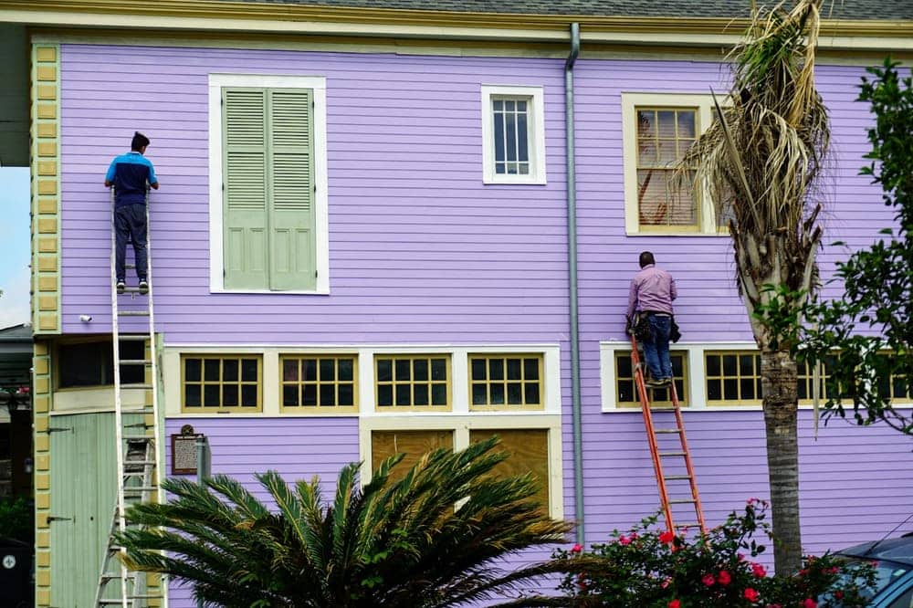 Two painters on ladders repainting a two-story house exterior
